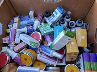 Box filled with multiple aromatherapy sprays, essential oil bottles, and candle tins including yellow and red round tins and spray bottles with purple and white labels.