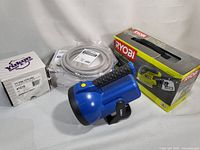 Overview photo showing Ryobi sander in box, blue flashlight, white auto part box, water filtration component and coiled fridge hose