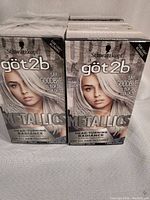 Six boxes of Schwarzkopf Got2b Metallic Silver permanent hair color arranged in two rows. Boxes feature a model with metallic silver hair and contain 1 application each.