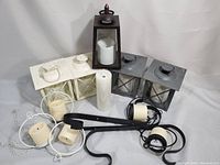 Various QVC home decor lights including three metal lanterns with candles and two black metal ceiling pendant lights with cream bulb sockets.