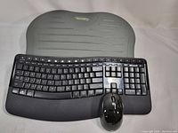 Top view of Microsoft wireless black ergonomic keyboard, black wireless mouse, and gray Kensington foot rest with visible small crack on surface.