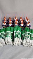Front view of a large group of green Expo2 dry erase markers lying down with Elmer's glue bottles with orange caps standing behind them.