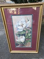 Full view of signed magnolia floral artwork matted in burgundy and teal, framed in heavy ornate gold frame