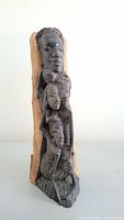 Front-right view of the hand carved African wooden sculpture showing stacked faces and natural wood back.