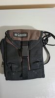 Front view of Columbia side bag, showing black and brown fabric, Columbia logo patch, and buckle closure