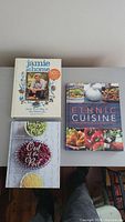 Three hardcover cookbooks laid flat: 'Jamie at Home' by Jamie Oliver, 'Ethnic Cuisine', and 'Out of the Rod' by Vicky Jones with images of beans and lentils on the cover.