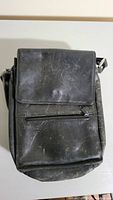 Front view of the black leather purse showing flap closure and front zipper pocket with visible wear and scuffs.