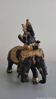 Side angle view of Buddha sculpture sitting on elephant figurine, showing gold and black paint detail and ornate decorations.
