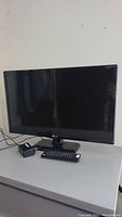 Front view of LG 24 inch flat screen TV with remote and power adapter on table.