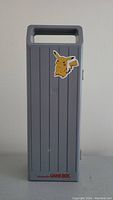 Front view of light gray Nintendo Game Boy carrying case featuring vertical grooves and Pikachu sticker on side.