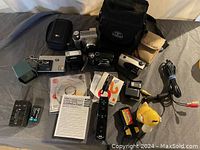 Overview of assorted cameras, flashes, camera bags, video game controllers, cables, chargers, batteries, and manuals.