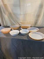 Seven pieces of CorningWare and Fire King bakeware displayed together on table with curtain background