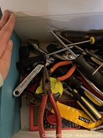 Box of assorted hand tools including pliers, screwdrivers, adjustable wrench, utility knife, tape measure, and multimeter.