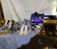 Photo showing eleven pairs of women's shoes in size 9-10 arranged in front of a white sheet, including a variety of sandals, wedge heel shoes, ankle boots, and some shoes still in boxes.