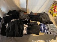 Photo showing a variety of folded pants, jeans, and leggings in black, gray, blue, and striped patterns.