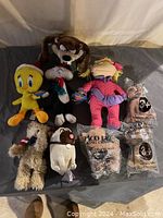 Overview of several plush toys including Looney Tunes characters Tweety, Taz, Sylvester, a Justin Bieber plush in pink, and three Taco Bell dog plush toys in original packaging on black surface.