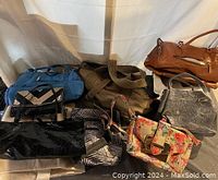 Photo showing eight purses and handbags of different colors, sizes, and materials spread on a surface.