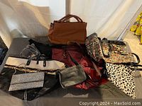 Overview of all seven purses and handbags together on a black surface against white background, showing variety of styles and colors.