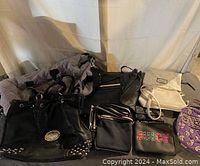 Overall view of seven purses and handbags including a studded black bag, white Steve Madden bag, Juicy pouch, and black crossbody bag.