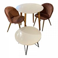 Two pink velvet chairs and two round white tables, the larger table has wooden legs, smaller table has black metal legs.