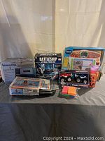 Wide view of assorted boxed toys and games on table including Battleship Star Wars model, Vtech toy, LeapFrog system, toy cars and foam blocks