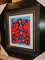 Framed vibrant art print showing abstract Thunderbird and figures in bold red, blue, black, purple colors in a black frame with white and black matting.