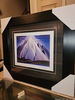 Angled view of professionally framed fine art print by Lawren Harris showing the mountain scene and black frame with protective corner covers