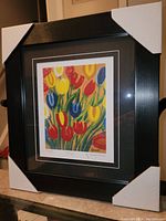 Framed colorful tulips print by Maud Lewis with protective corner covers on frame.