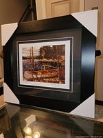Framed fine art print showing a canoe in nature with thick black matte frame.