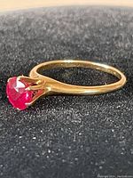 Side view of the 14 Kt gold ring showing the bright red round stone in a claw setting.
