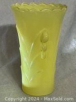 Front view of yellow glass vase showing embossed floral design and scalloped top edge.