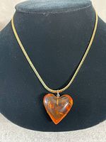 Full front view of amber heart pendant on gold choker necklace displayed on black bust.
