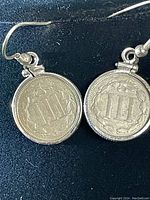 Close-up photo showing the back side of the two earrings featuring the Roman numeral III with wreath design on US 3 cent nickel coins.
