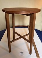 Front view of mid-century teak folding side table showing round top and straight legs with cross support.