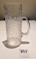 Clear glass pitcher with textured bubble pattern and handle, photographed on white surface with lot tag.