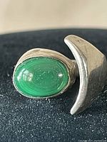 Close-up view of polished oval green stone set in sterling silver ring with curved design detail.
