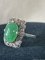 Close-up front view of ornate sterling silver ring with large oval green jade stone and marcasite decorated border.