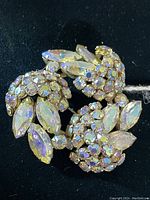 Front view of the gold plated Sherman brooch showing array of aurora borealis rhinestones in round and marquise shapes arranged in a circular floral pattern.