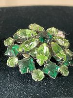 Close-up photo of the brooch showing the multi-shape green rhinestones and silver-tone setting.