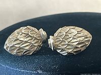 Close-up photo of the side view of the two sterling silver acorn earrings showing textured scale pattern and rounded acorn cap tops with earring closures.