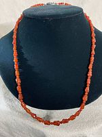 Front view of a red-orange carnelian stone bead necklace displayed on black bust, showing the bead shapes and overall length.