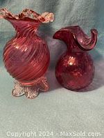 Two cranberry glass vases displayed side by side against fabric background