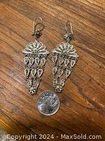 Full view of both earrings placed flat on wooden surface next to a quarter for scale.