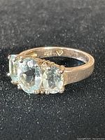 Close-up of the ring from an angle showing the three aquamarine stones and sterling silver band with triangular 'F' stamp.