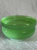 Side angle showing glossy jadeite green glass candy bowl with smooth finish on a light fabric background.