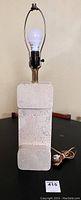 Front view of vintage travertine table lamp showing geometric block stone base, brass socket, bulb, and wiring cord with switch.