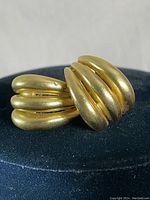 Close-up front view of gold-tone curved multi-bar clip-on earring showing shape and surface finish.