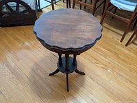Full view of antique round side table showing scalloped edge and tripod base with spindle legs and circular shelf.