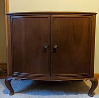 Front view of the antique Victorian cabinet showing two paneled doors, lock, and round handles on curved legs