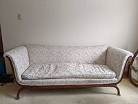 Full view of Victorian sofa upholstered in pale fabric with carved wooden base and legs.